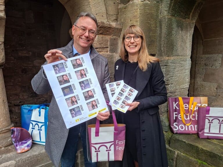 Ab sofort im Kulturbüro erhältlich: limitierte Sonderbriefmarken mit exklusiven Motiven der Kreuzgangspiele 2026 und die neue Kollektion der beliebten Kreuzgangspiele-Taschen. Herbert Lindörfer, Vorsitzender des Fördervereins, zeigt die Marken in vergrößerter Darstellung, Kulturbüro-Leiterin Dr. Maria Wüstenhagen präsentiert den 10er-Bogen im Originalformat.